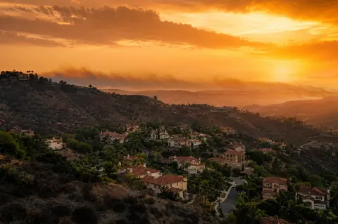 Hillside neighborhood in the San Fernando Valley at dusk with dry chaparral hills and smoky haze on the horizon