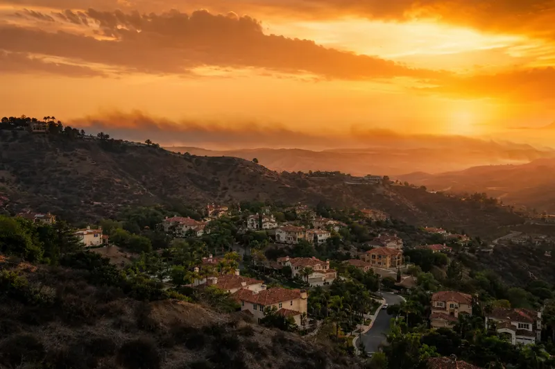 Hillside neighborhood in the San Fernando Valley at dusk with dry chaparral hills and smoky haze on the horizon