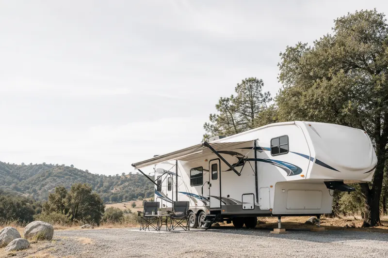 Fifth-wheel travel trailer parked and leveled at a quiet campsite under soft daylight, representing RV insurance for parked and towed vehicles